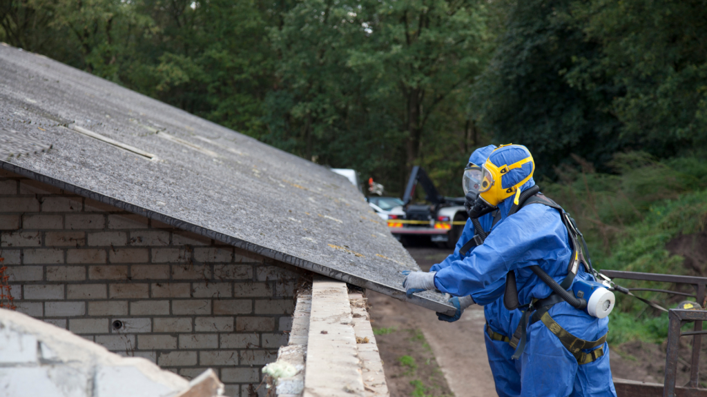 Asbestos Removal Worker in Protective Gear Worker in blue protective suit and mask inspecting asbestos material on a roof.